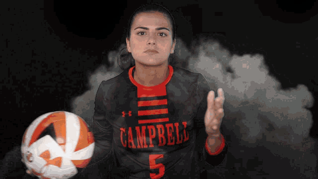 a girl wearing a campbell jersey holds a volleyball