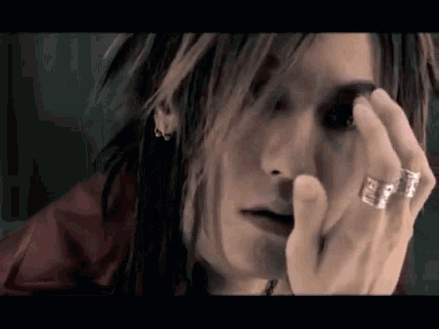 a woman with long hair and rings on her fingers is covering her eyes with her hand .