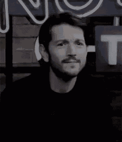 a man with a beard is standing in front of a neon sign .