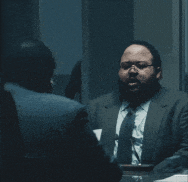 a man in a suit and tie talking to another man with the words " there 's a coffee maker " above him