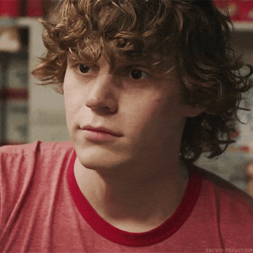 a young man with curly hair is wearing a red t-shirt with a red ring around the neck