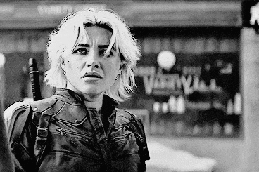 a black and white photo of a woman holding a gun in front of a building .