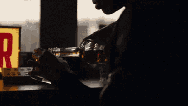 a man holds a bottle of alcohol in front of a sign that says ' r ' on it