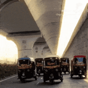 a row of rickshaws are driving under a bridge and one of them has the word rickshaw on it