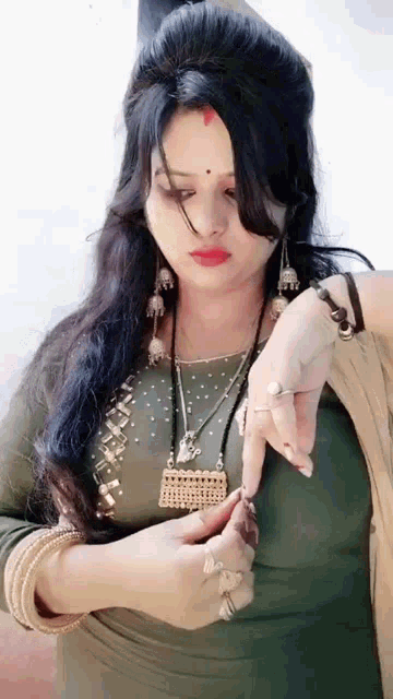 a woman wearing a necklace and earrings is looking at her watch while standing .