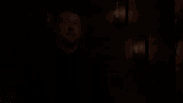 a man in a black suit is standing in a dark room with his eyes closed and a plant in front of him .