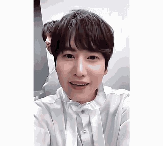 a young man in a white shirt is smiling and looking at the camera .