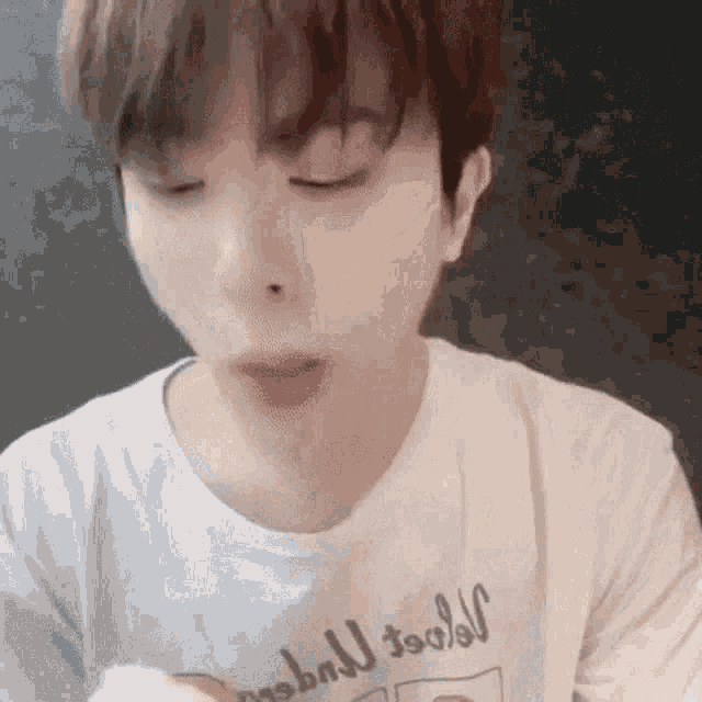 a young man wearing a white t-shirt is eating a sandwich with his eyes closed .