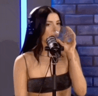 a woman is drinking water from a glass while standing in front of a microphone .