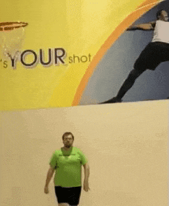 a man in a green shirt is playing basketball in front of a sign that says " your shot "