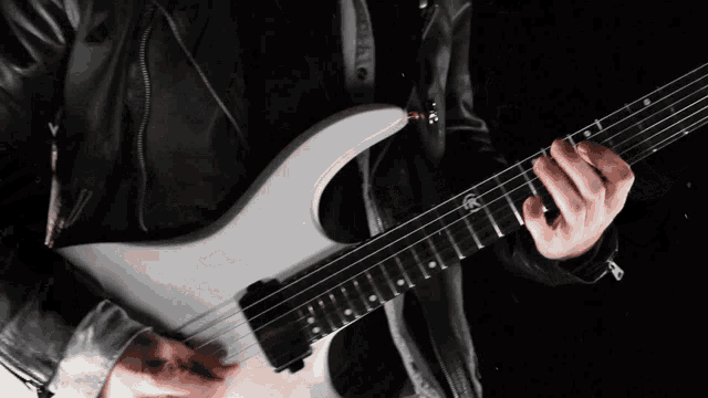 a man is playing a white electric guitar with a black jacket on