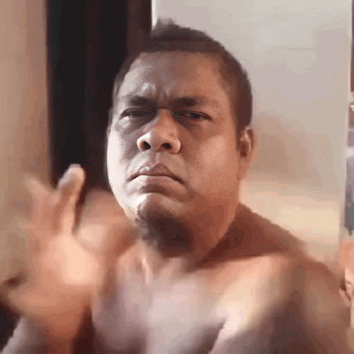 a shirtless man is making a funny face and waving his hand in front of a mirror .