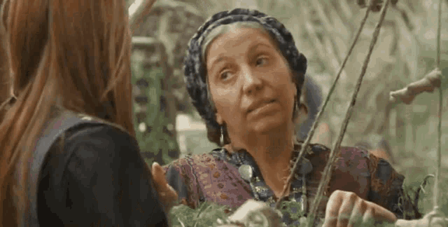 a woman is talking to another woman while holding a plant in her hands .
