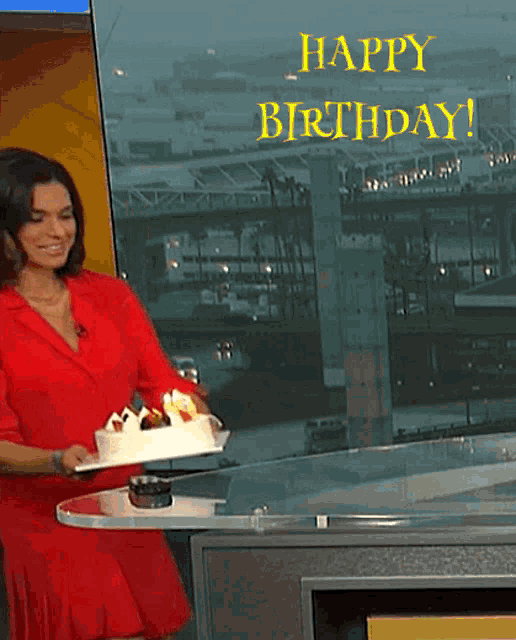 a woman in a red dress is holding a birthday cake in front of a happy birthday sign