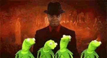 a man in a suit and hat is standing next to three green kermit the frogs