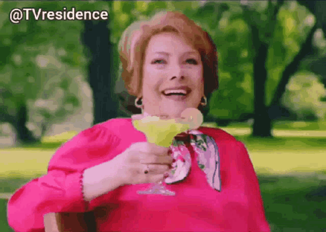 a woman in a pink shirt is holding a margarita in her hand and smiling