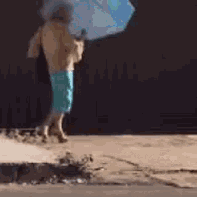 a shirtless man in blue shorts is holding an umbrella while walking down the street .