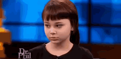 a little girl is standing in front of a blue screen with the word dr phil on it .