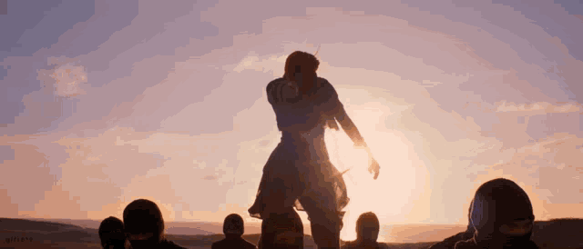 a group of people are standing in front of a sunset in a desert .