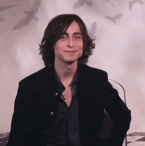 a young man with long hair is wearing a black jacket and smiling .