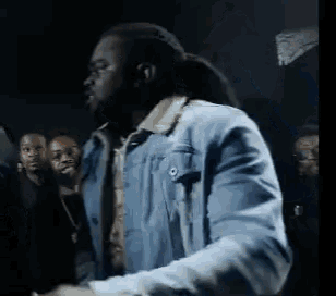a man wearing a blue denim jacket is standing in front of a crowd .
