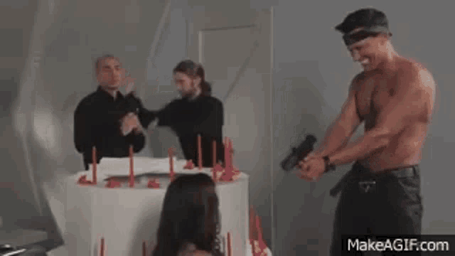 a man is standing in front of a cake with candles and holding a gun .