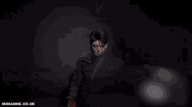 a man is kneeling down in a dark room with the website numanme.co.uk written on the bottom right