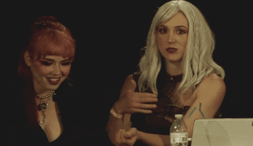 two women are sitting next to each other and one has a bottle of water in front of her