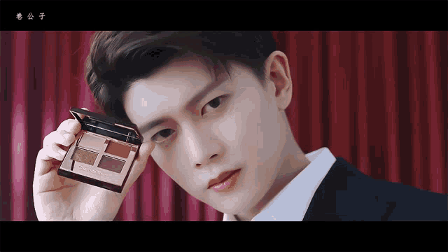 a man in a suit is holding a palette of eye shadow