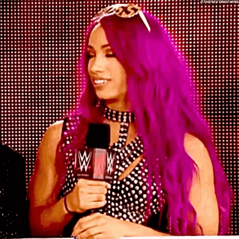 a woman with purple hair is standing in front of a microphone and smiling .
