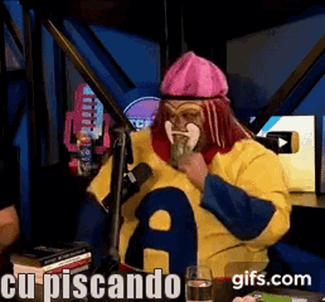 a man with red hair and a pink hat is sitting in front of a microphone with the words cu piscando on the bottom