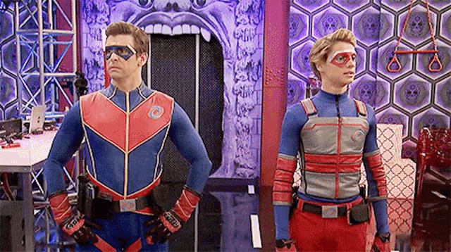 two men in superhero costumes are standing next to each other in front of a skull wall .