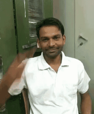 a man in a white shirt is smiling and waving his hand in front of a green cabinet