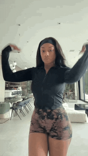 a woman wearing shorts and a headband is standing in a living room with her arms outstretched .