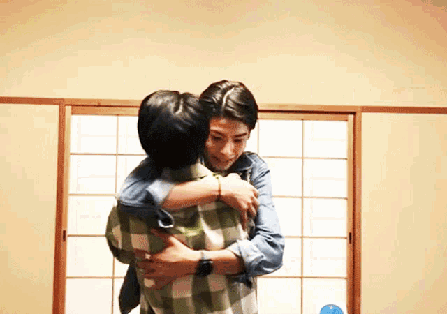 a man in a plaid shirt is hugging another man in a denim shirt