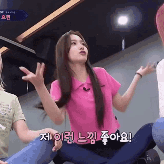 a girl in a pink shirt is sitting on the floor with her hands in the air
