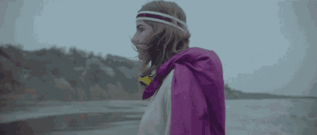 a woman wearing a purple cape and a headband is standing on a beach .