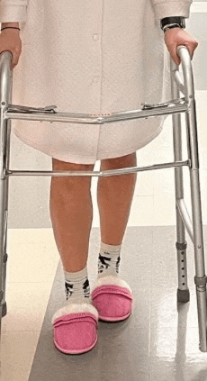a woman is using a walker in a hospital while wearing pink slippers .