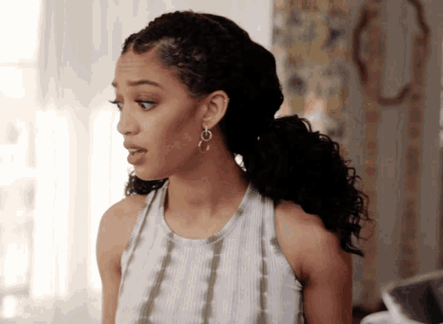 a woman with curly hair wearing a white tank top and earrings