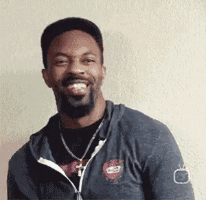a man with a beard is smiling while wearing a hoodie and a necklace .
