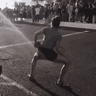 a man is standing on one leg on a street in front of a crowd of people .
