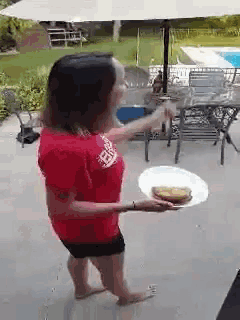 a woman in a red shirt is holding a white plate with a sandwich on it