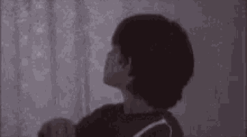 a person is standing in front of a window in a dark room with a light shining through it .
