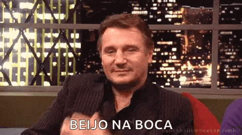 a man in a suit is sitting in front of a window with the words beijo na boca written on it