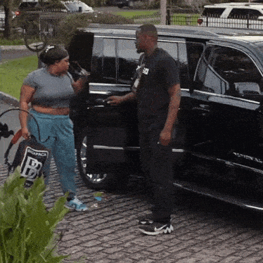 a man in a black shirt with the letter b on it stands next to a woman in blue sweatpants