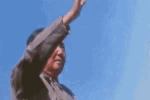a man is standing in front of a blue sky with his hand up in the air .