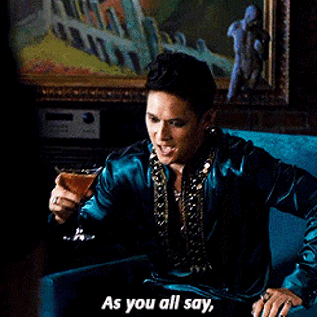 a man in a blue jacket is holding a glass of beer and says as you all say