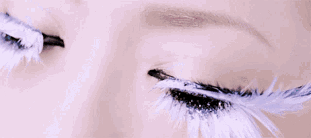 a close up of a woman 's eyes with white feathers and glitter
