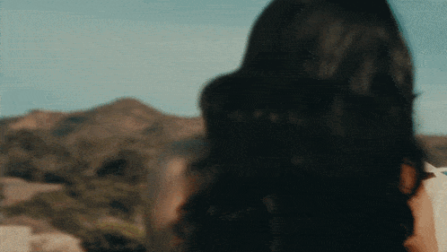 a woman with long dark hair is standing in front of mountains