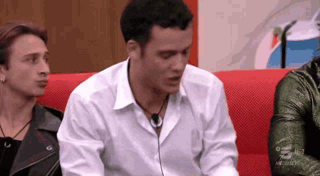 a man in a white shirt is sitting on a red couch with other people